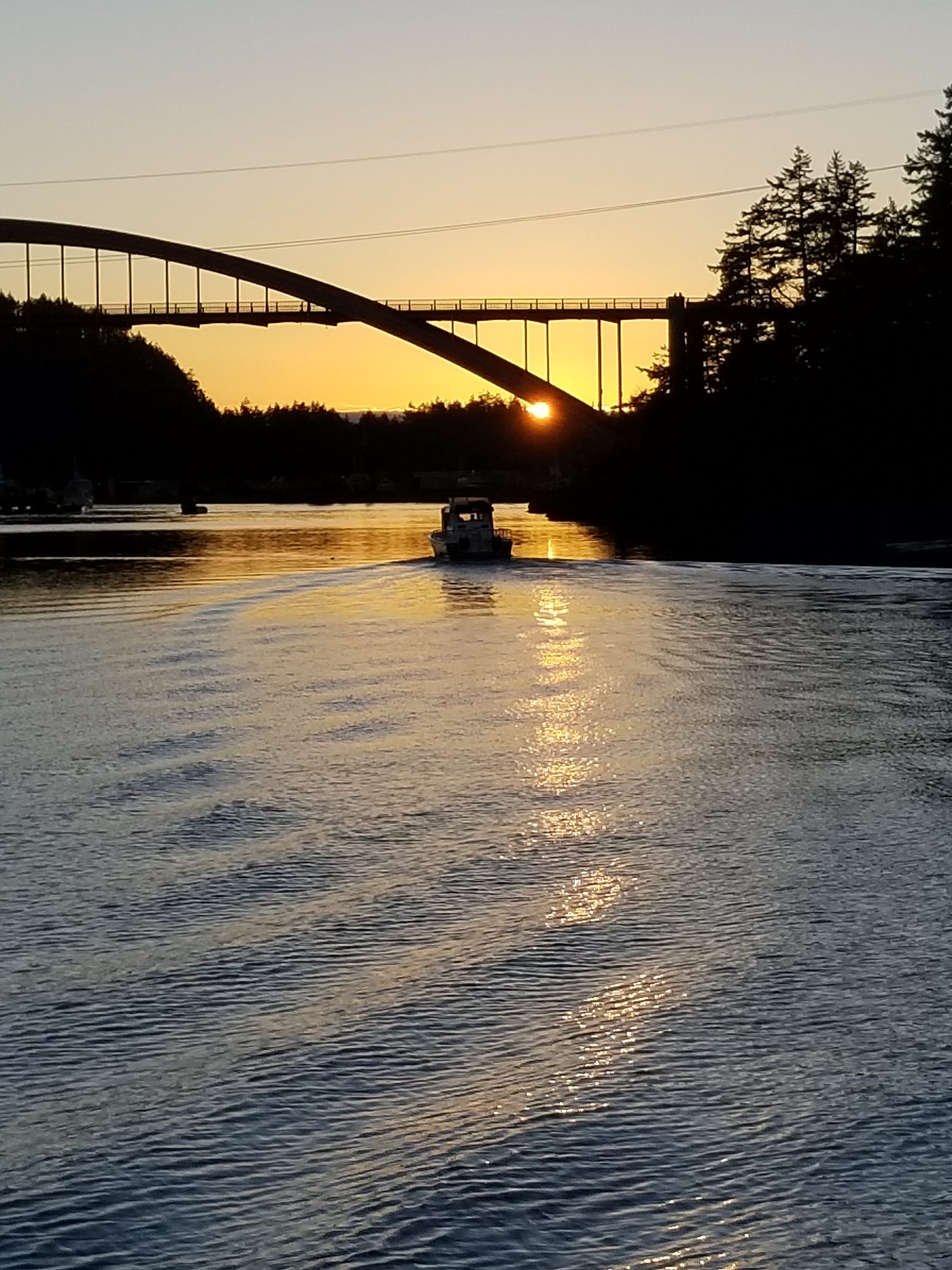 sunset beneath a bridge in shadow, a boat in the channel