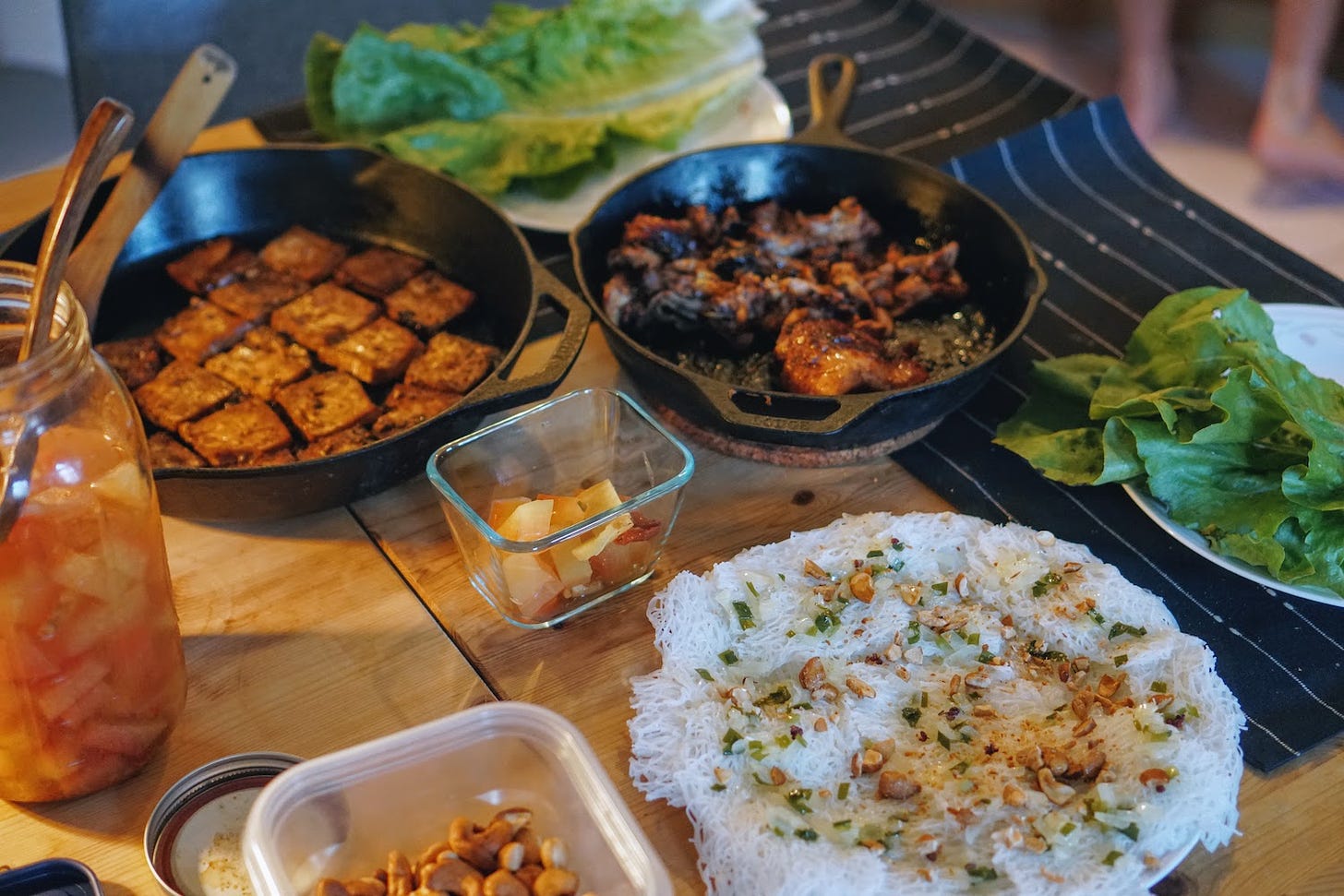 A table filled with plates of vermicelli, tofu, chicken, lettuce and pickles