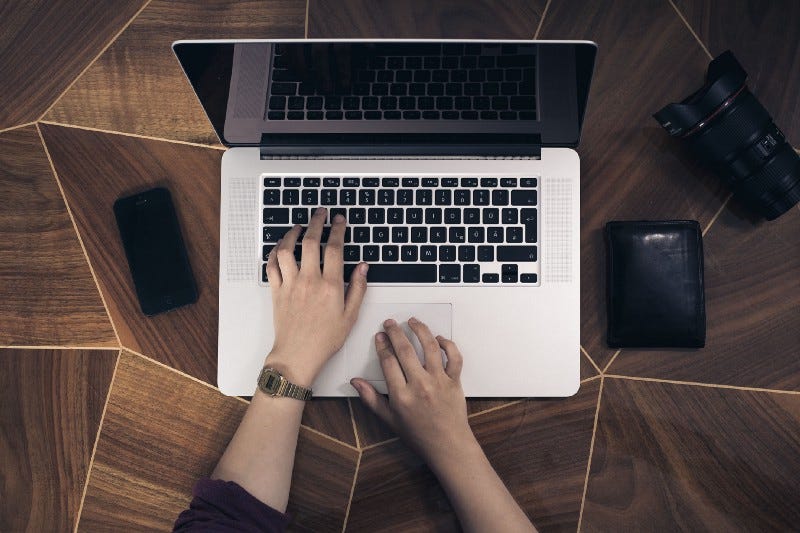 image of a writer’s hands resting on a desk with a macbook for article titled “write for the creative mind”