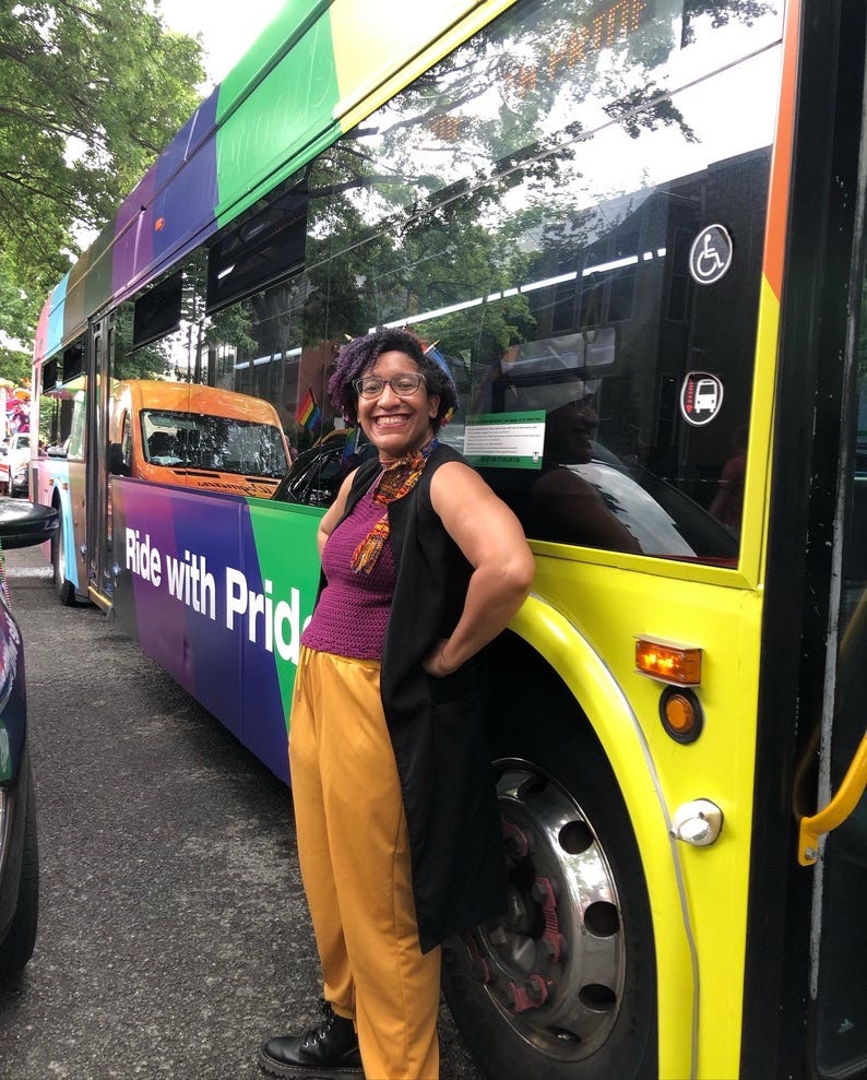 Kristen in the nonbinary flag colors, leaning against a WMATA metrobus wrapped in the progress pride flag colors