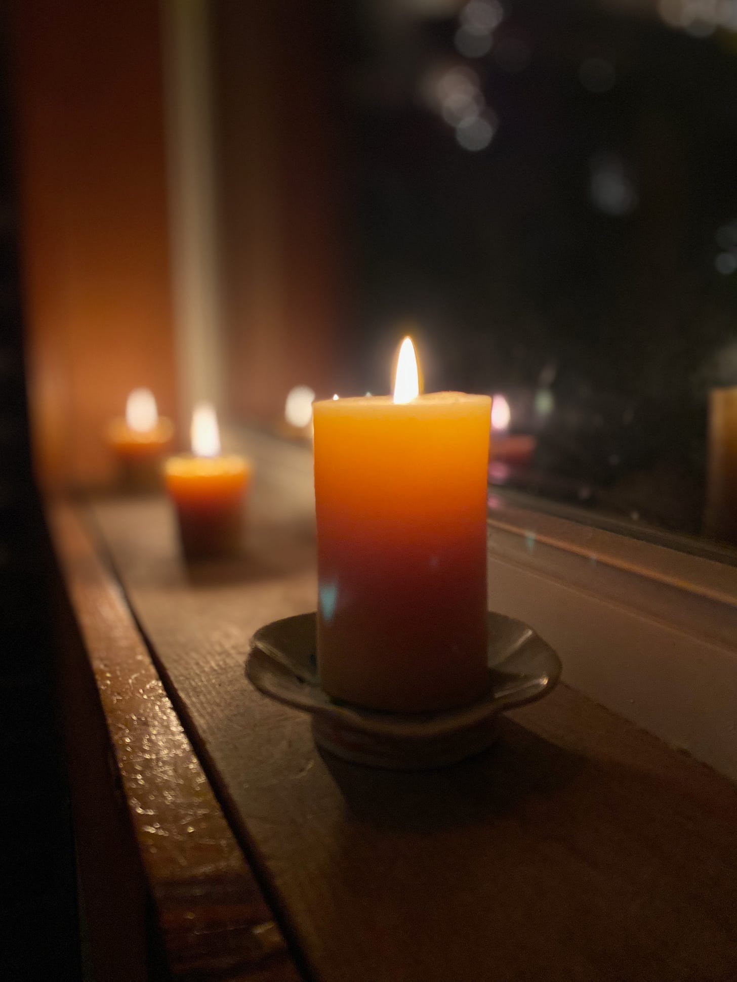 Three beeswax candles lined up on a windowsill, in front of a dark window.