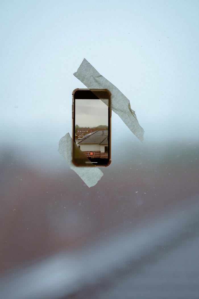 A phone taped to the window with a few pieces of tape instead of being held with something better.