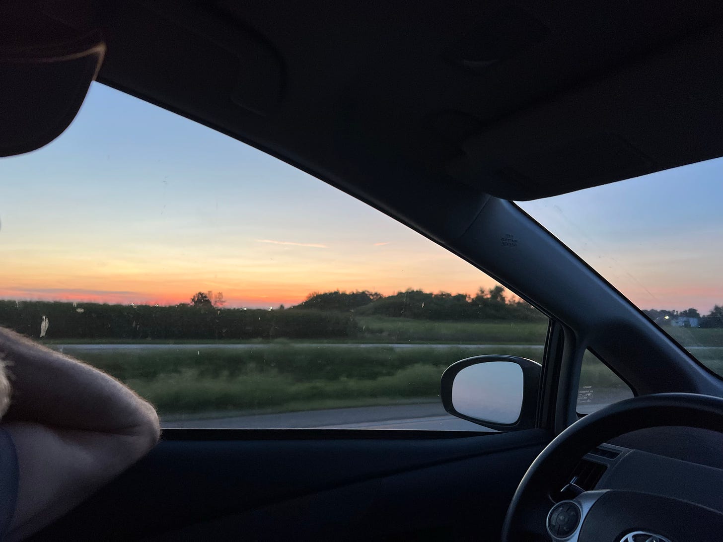 Vivid prairie sunset through a driver's side window of a car