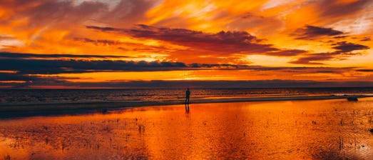 A man by a stretch of water watching a fiery sunset