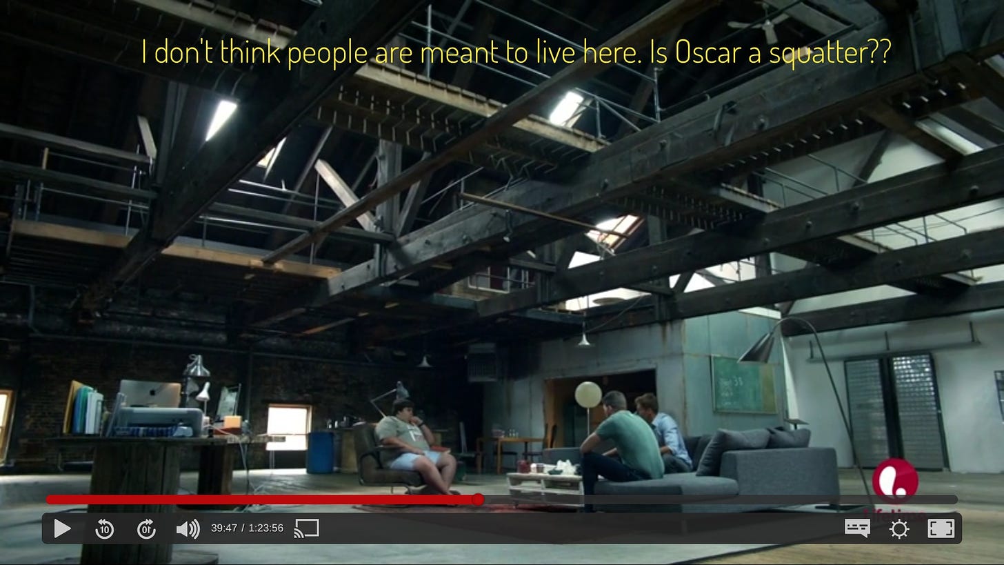 Three men sitting in the middle of a cavernous space with metal beams serving as the ceiling, and concrete everything, captioned "I don't think people are meant to live here. Is Oscar a squatter?"