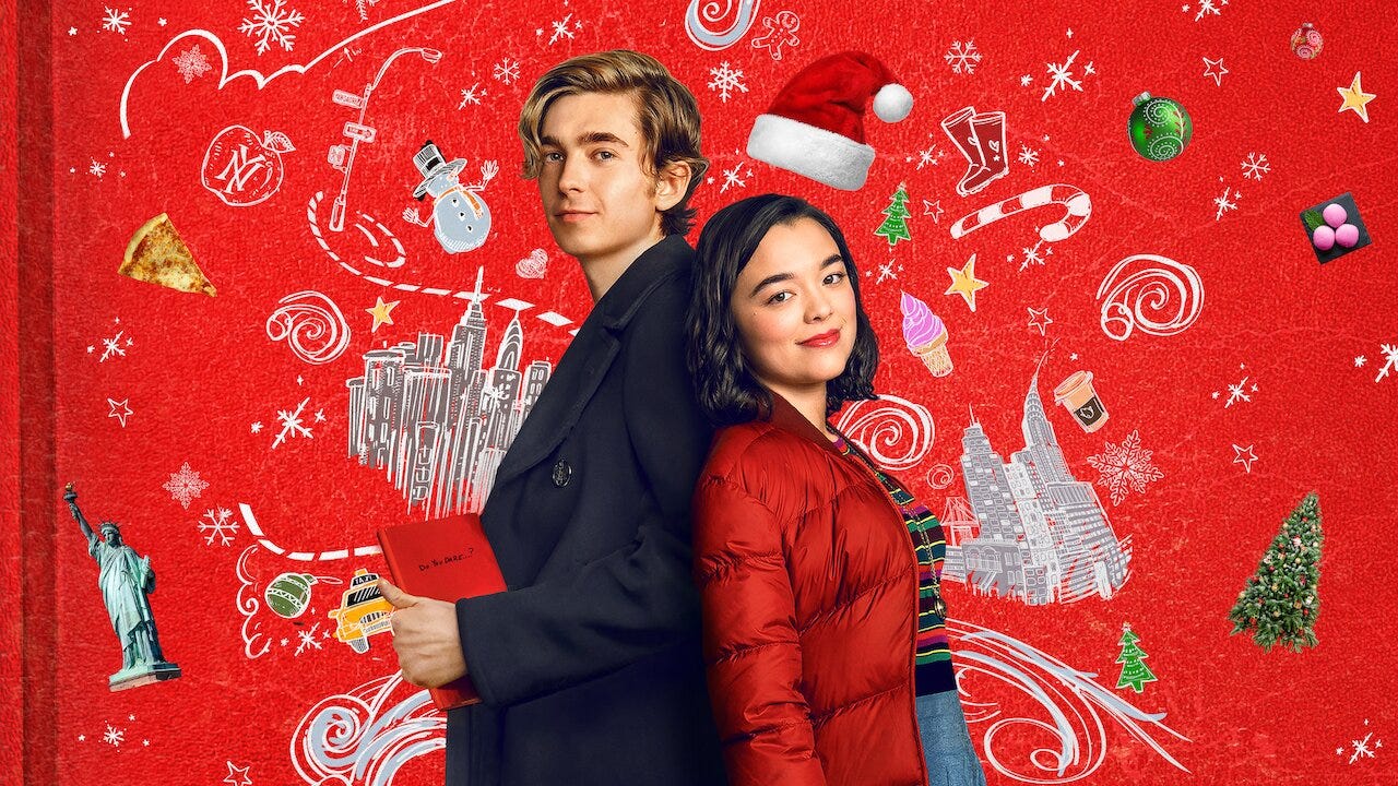 A teenage boy and girl stand back-to-back in front of a red notebook covered with Christmas and New York-themed doodles.