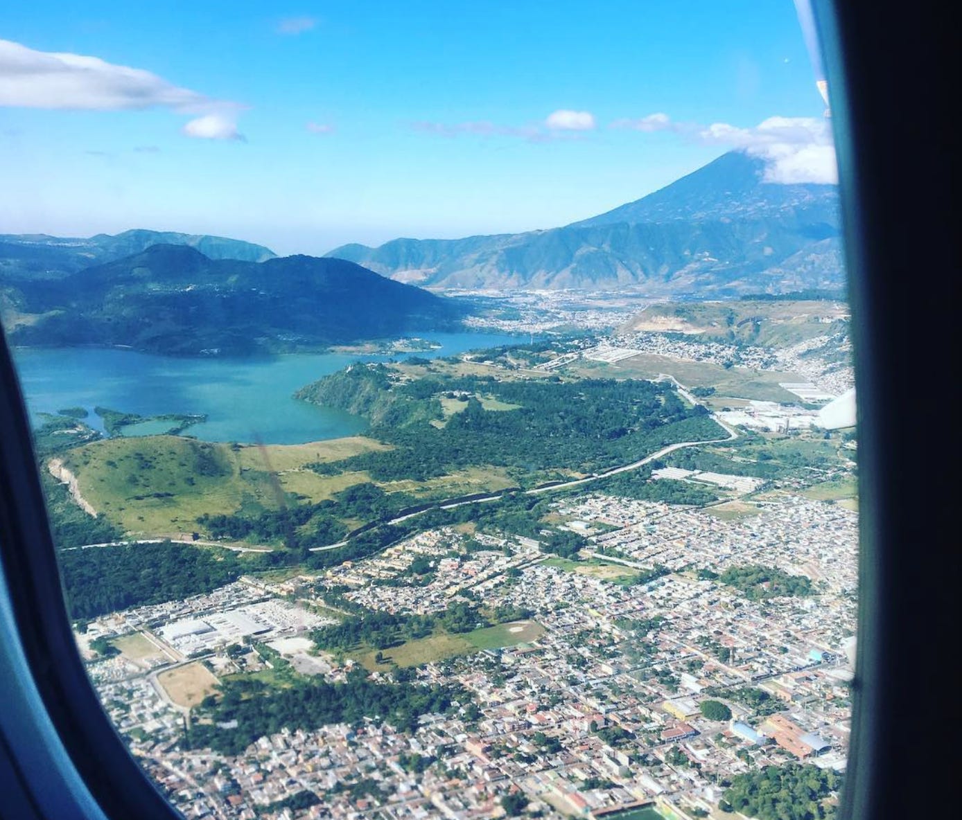 The view through an airplane window of Guatemala City with the water and mountains in the background.