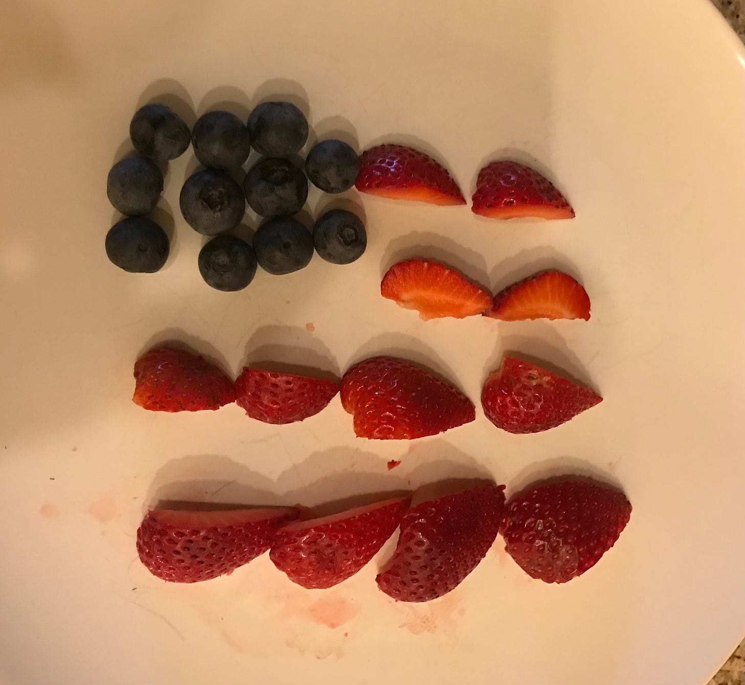 blurry image of a white plate with some blueberries and sliced strawberries, in a vague shape of an American flag