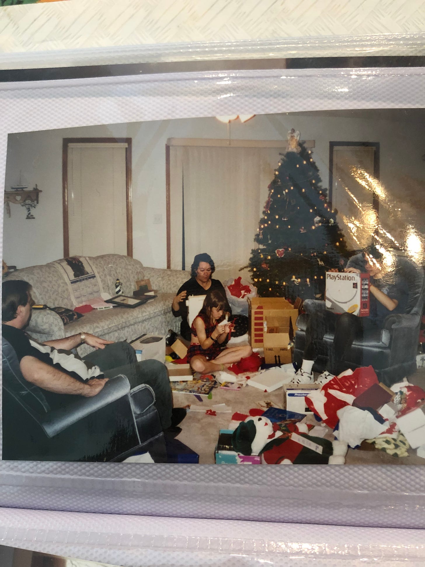 my family sitting with messes of presents around a Christmas tree. My mom is beside me, my dad is in a chair, and my brother sits in another chair. I'm looking intently at a present. 