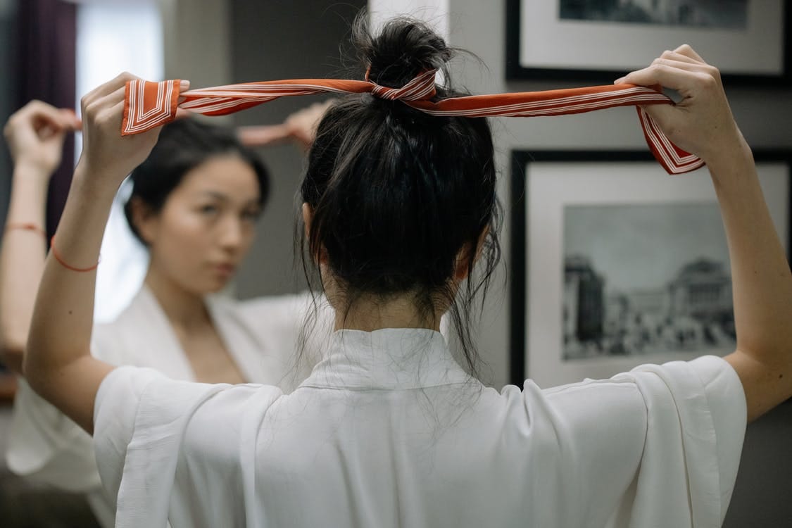 Close-Up Shot of a Woman in White Robe Tying Her Hair in front of a Mirror