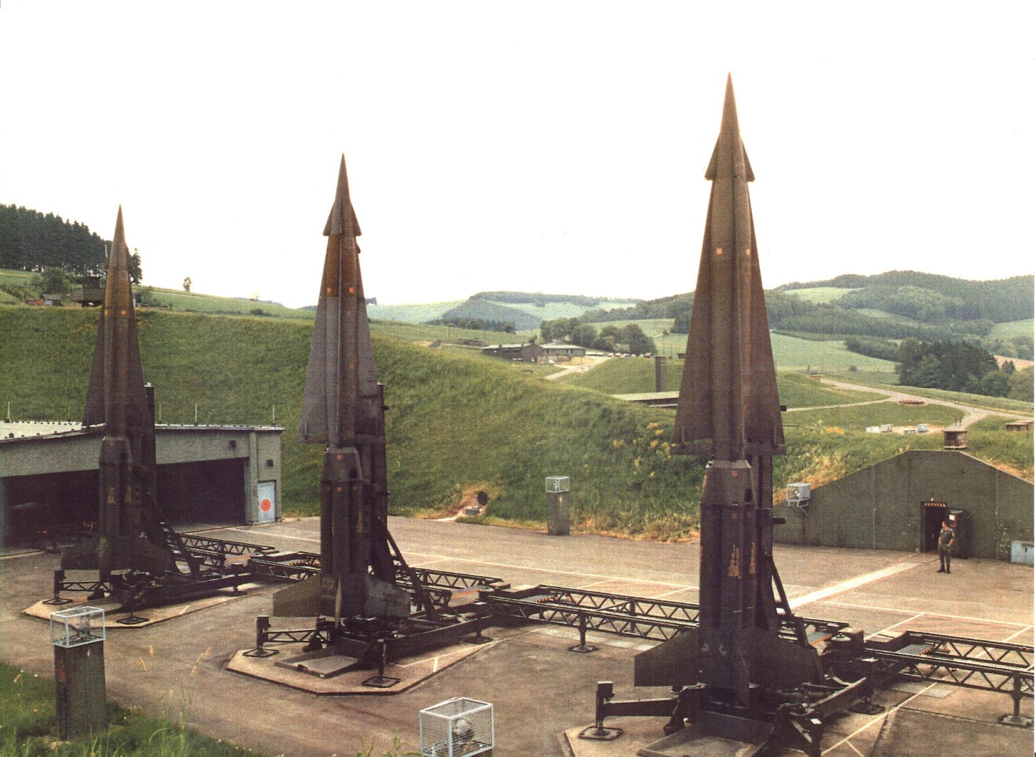 Drei aufgerichtete NIKE-Flugabwehrraketen in einer Raketenstellung in Oedingen, Nordrhein-Westfalen, 1980. Im Hintergrund ist die sommerliche Berglandschaft des Sauerlands zu sehen. Bild: August Freimuth via Wikimedia Commons