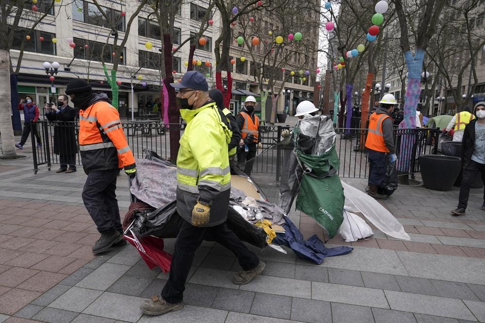 Workers carry a tent used by people experiencing homelessness to a garbage truck, Friday, March 11, 2022, during the clearing and removal of several tents at an encampment in Westlake Park in downtown Seattle. Increasingly in liberal cities across the country — where people living in tents in public spaces have long been tolerated — leaders are removing encampments and pushing other strict measures to address homelessness that would have been unheard of a few years ago. (AP Photo/Ted S. Warren)