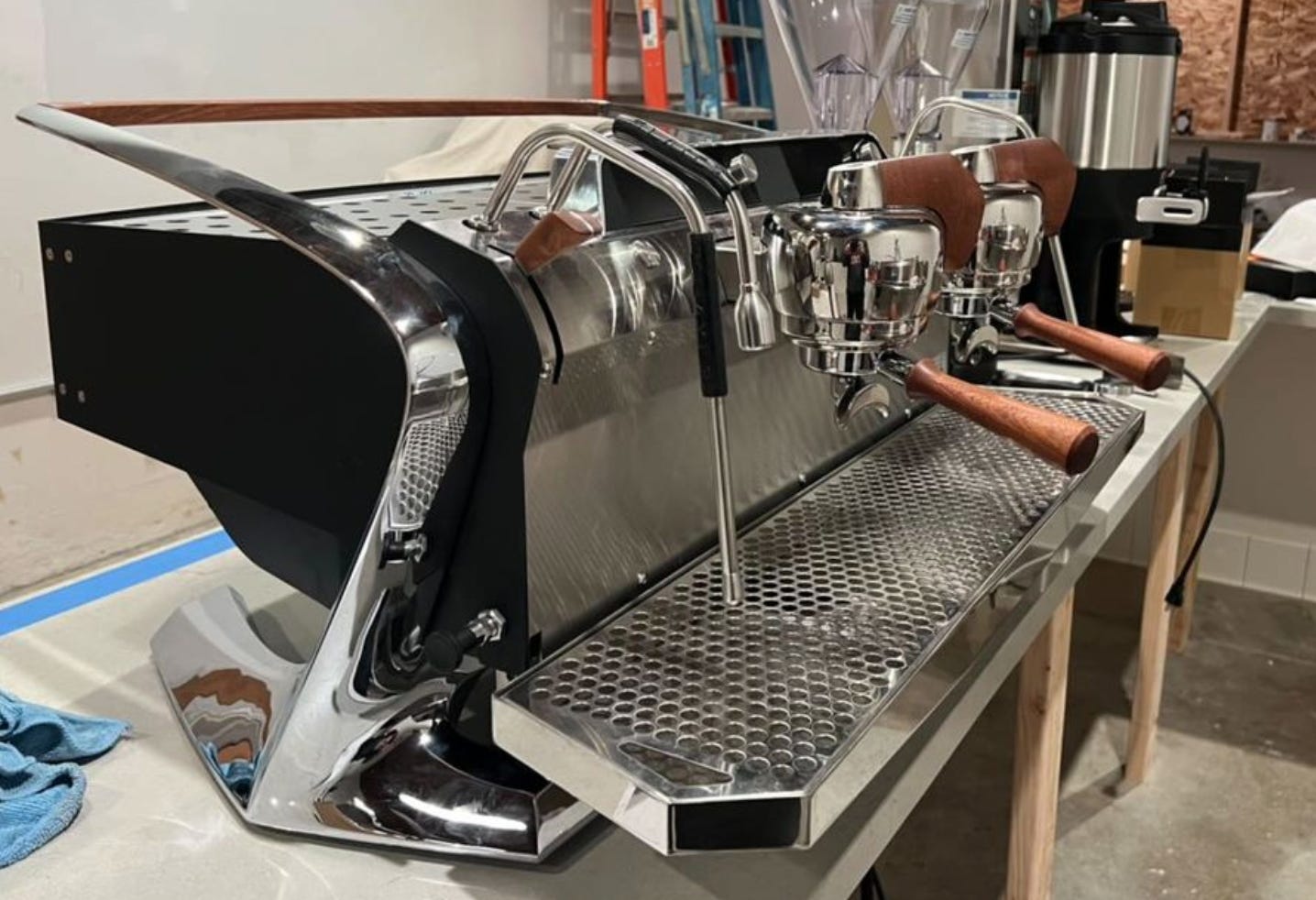A close-up of a stainless steel espresso machine with two portafilters with wood handles. The machine has black trim.