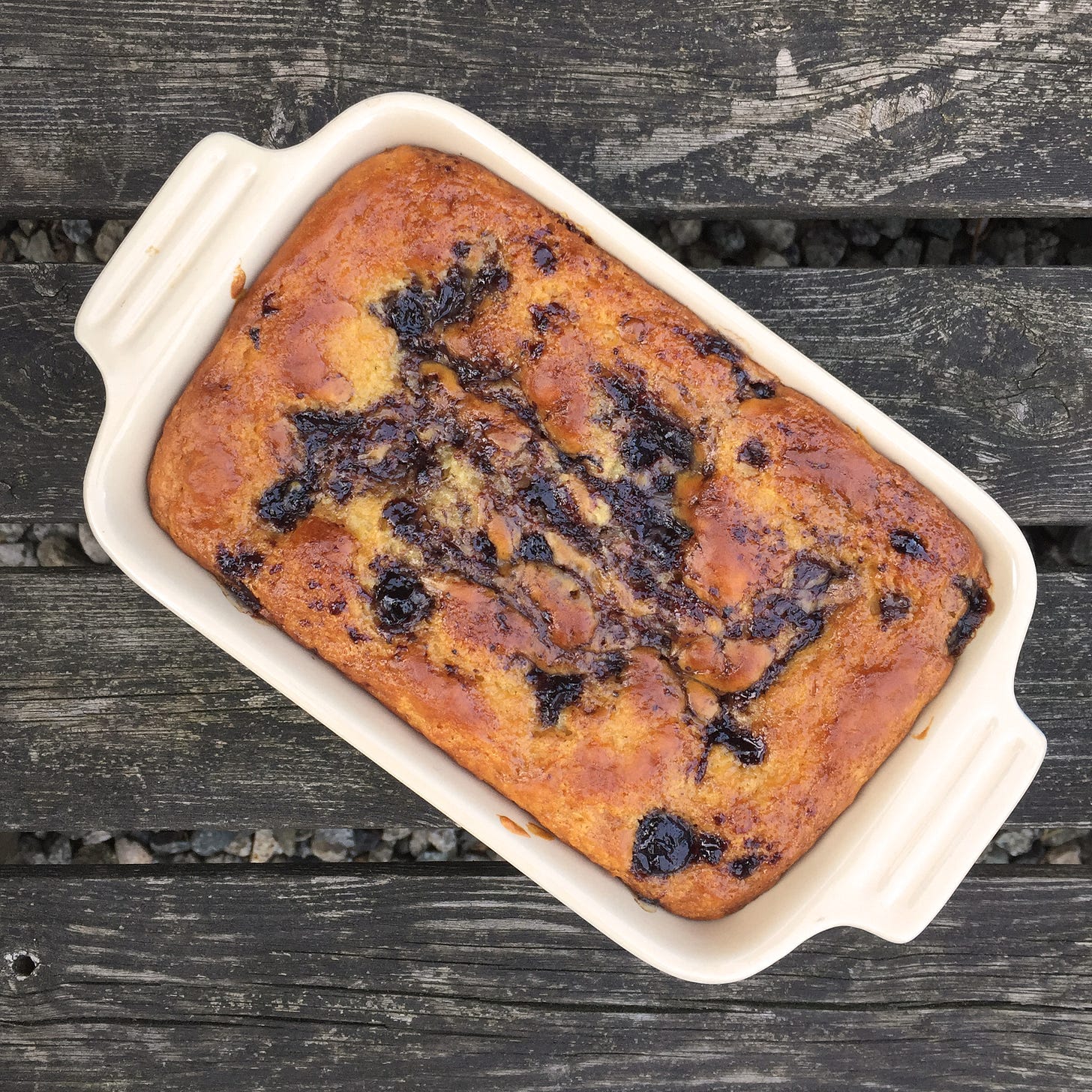 In a small glazed cast-iron loaf pan, a golden-brown cake with messy swirls of blueberry jam. 