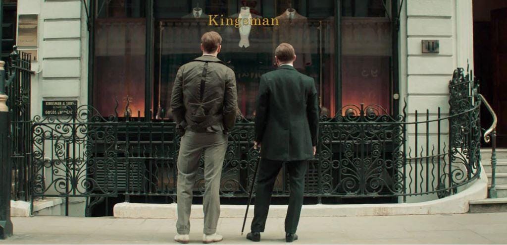 The Duke and Conrad stare into the Kingsman tailor shop, their backs to the camera.