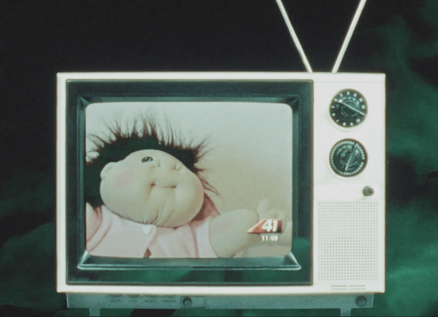 A TV shows a commercial for Cabbage Patch Kids dolls.