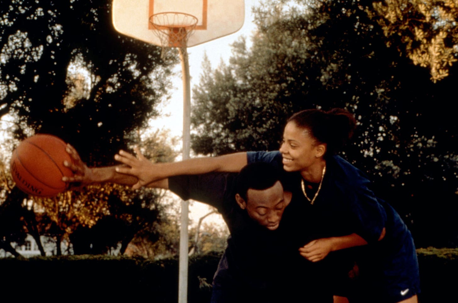 The two characters of love and basketball playing basketball. She is reaching over his back trying to grab the ball which he is holding at arm's length. 