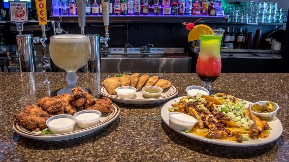 Three plates of fried appetizers flanked by a beer and a cocktail