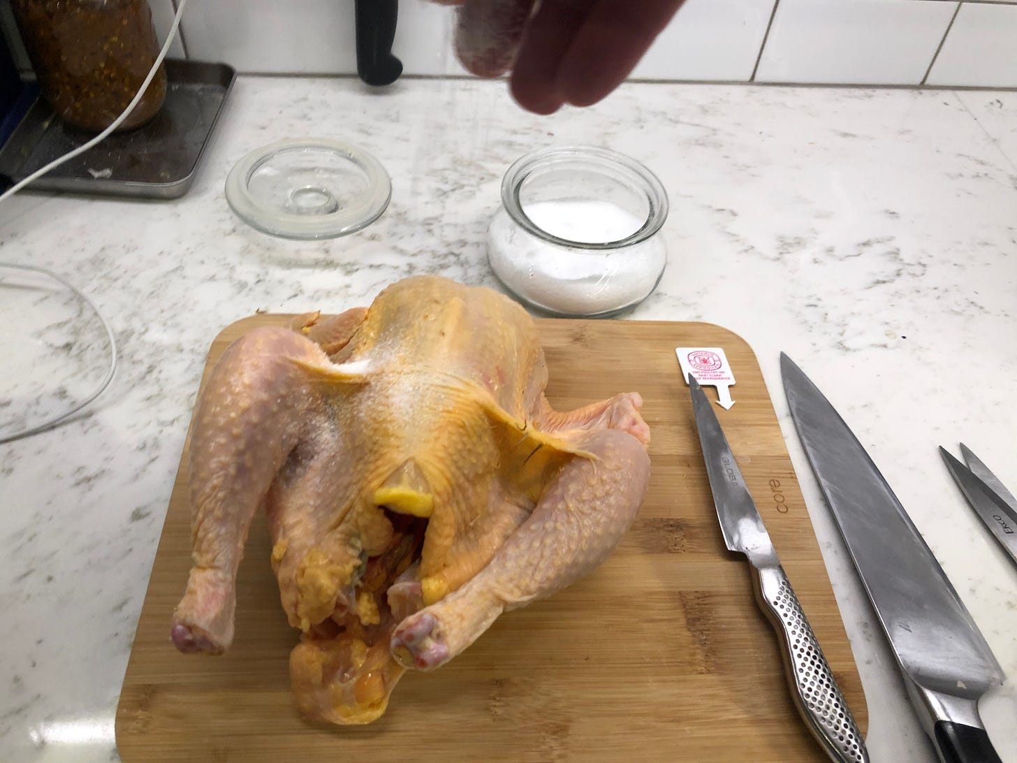 A hand sprinkling salt onto the chicken.