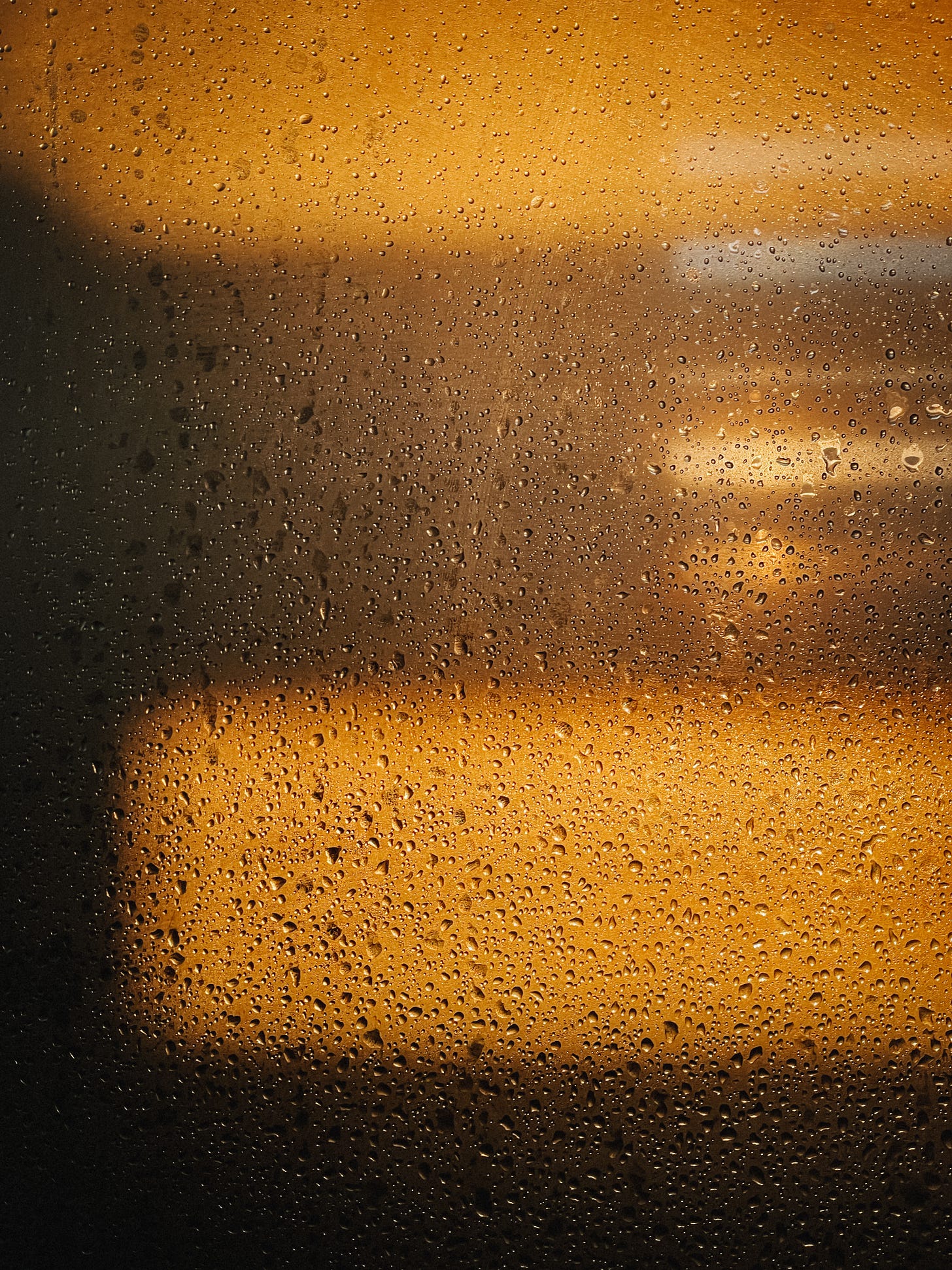 The wet glass of a shower screen, stripes of golden light shining through.