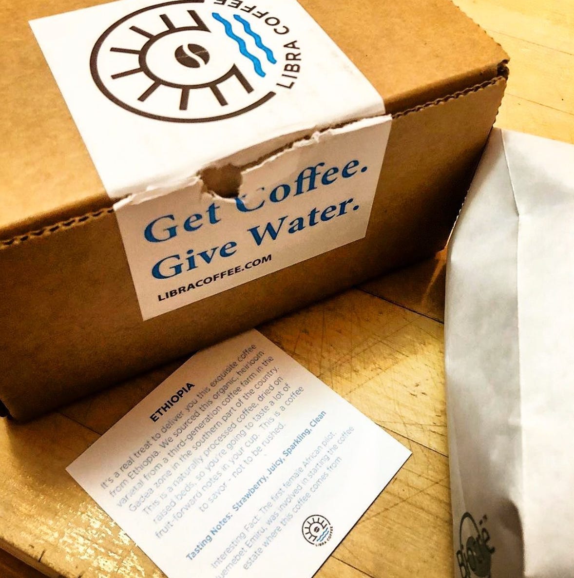 A brown cardboard box, small, with a packaging lable torn that says "Get Coffee. Give Water. Libra Coffee.com" and a description for the Ethiopia coffee inside.
