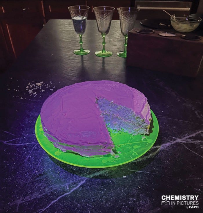 A cake with pink fluorescent frosting sitting on a green fluorescent plate, both glowing against a dark background.