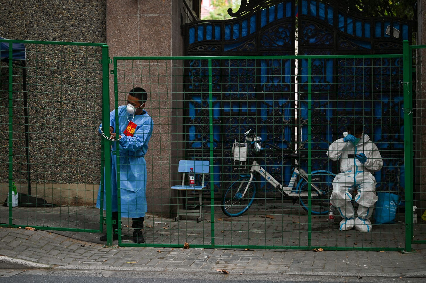 A worker wearing protective gear padlocks a fence to secure a residential area under a Covid-19 lockdown in the Xuhui district of Shanghai on June 16, 2022. (Photo by Hector RETAMAL / AFP) (Photo by HECTOR RETAMAL/AFP via Getty Images)