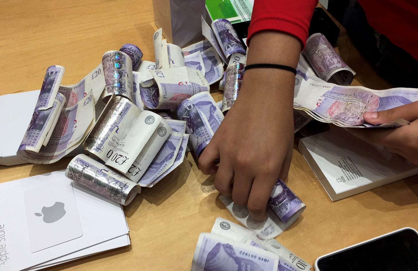 A shop assistant counts piles of British Pound Sterling banknotes at an Apple store in London