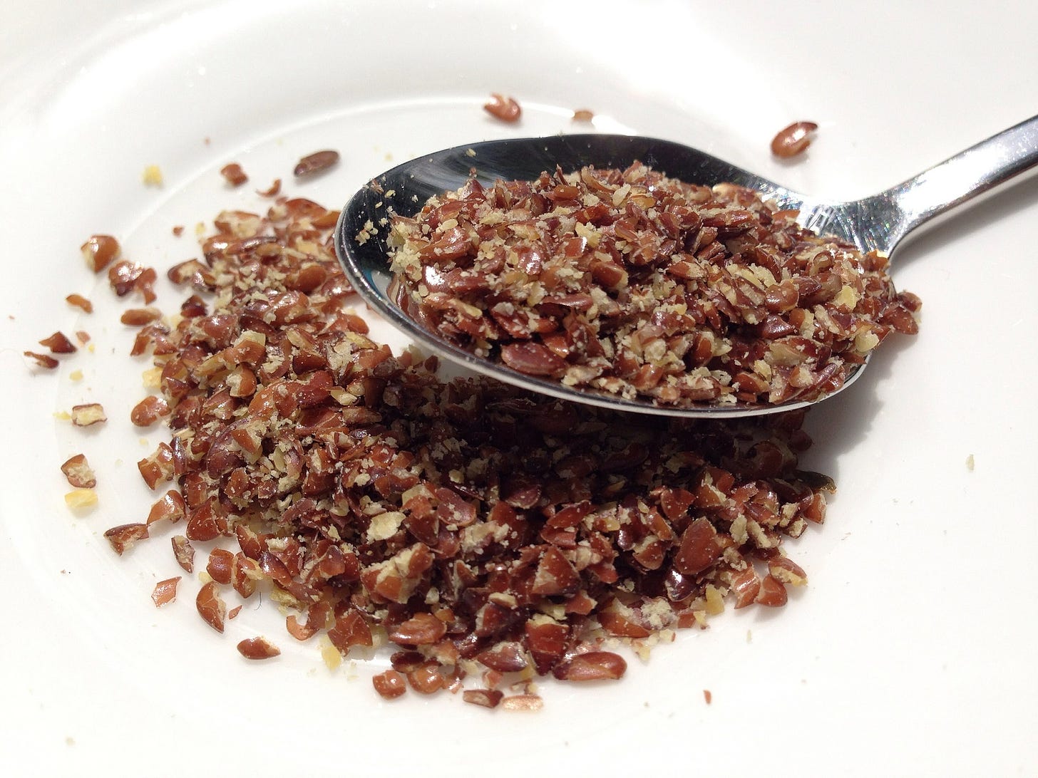 Broken flaxseeds in a spoon and on a plate