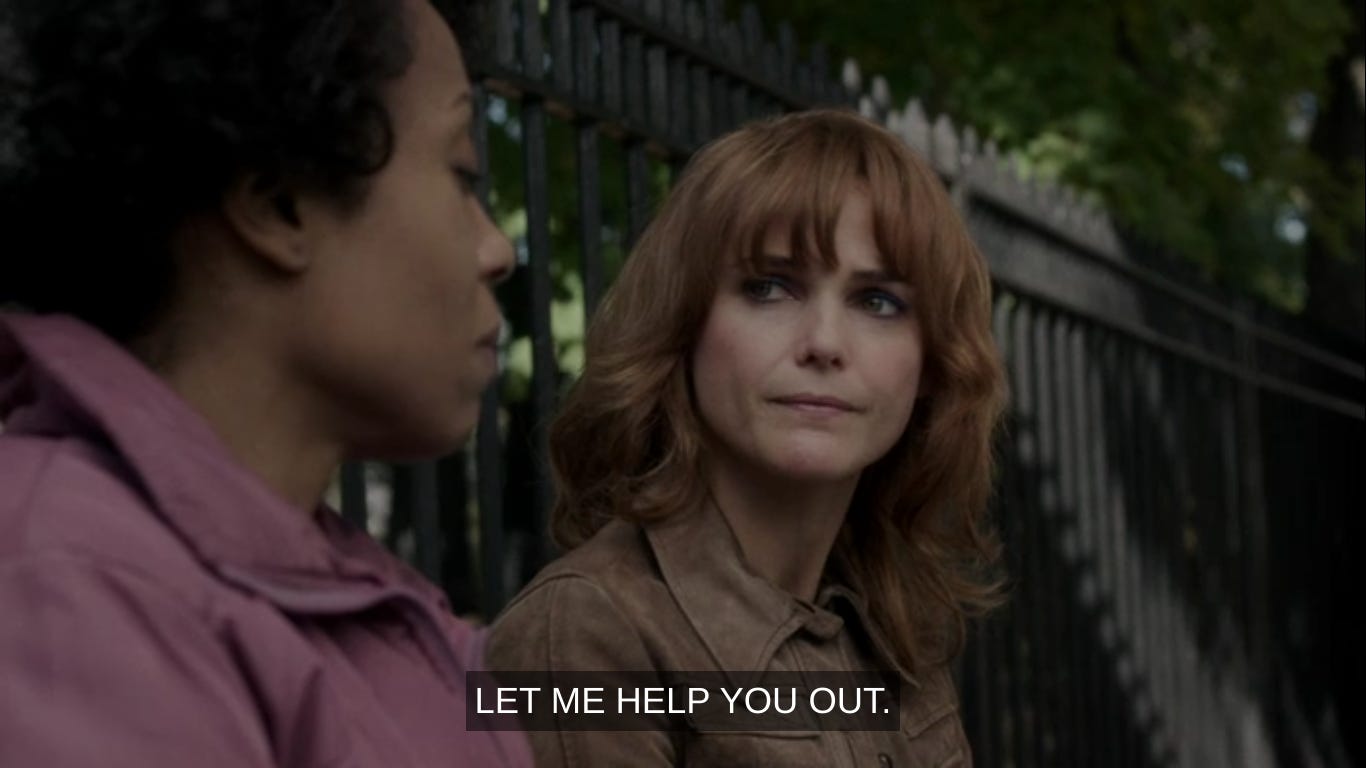 Elizabeth in a reddish wig saying to Lisa in front of a fence: "Let me help you out."