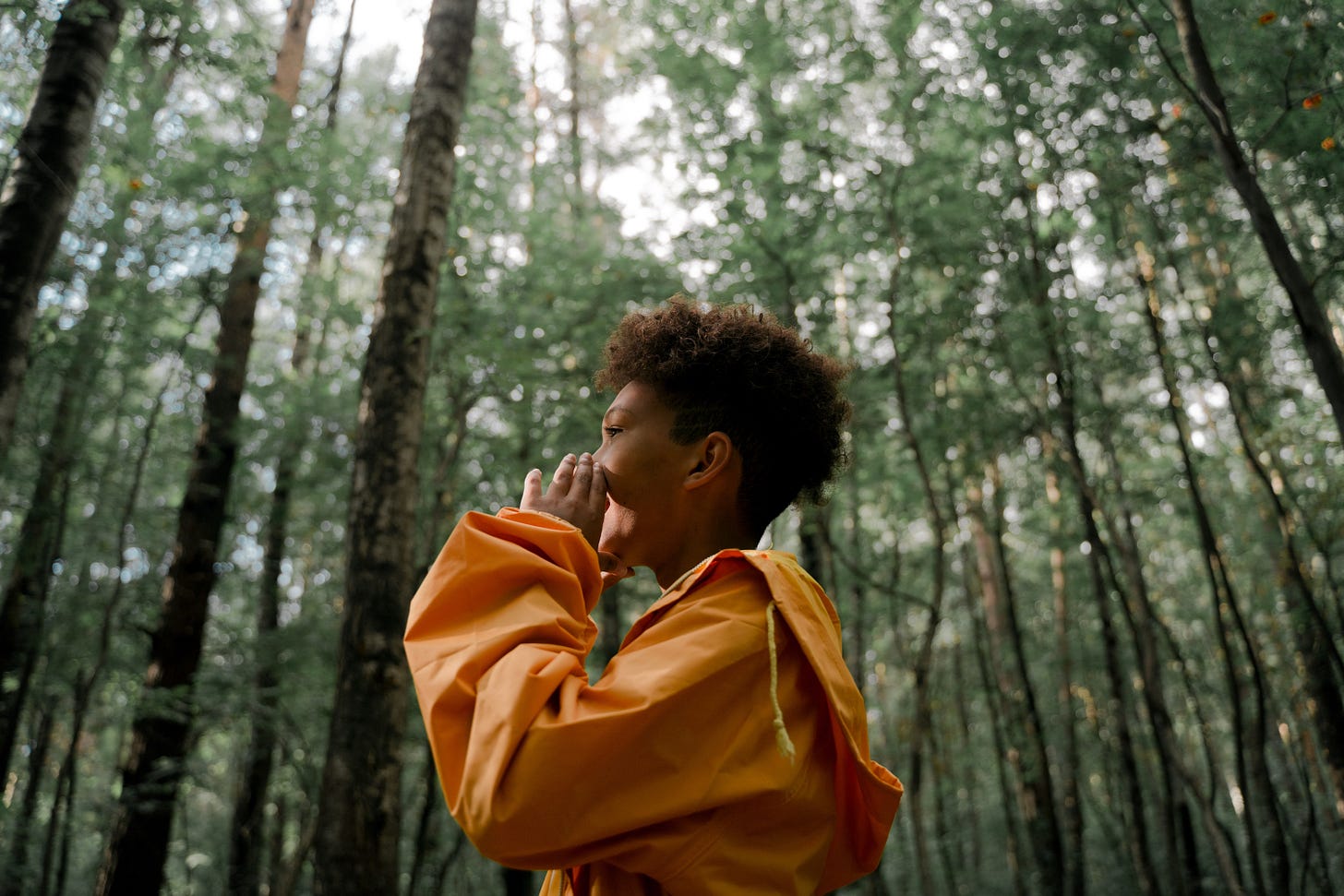 A boy in a yellow jacket shouting in a forest.