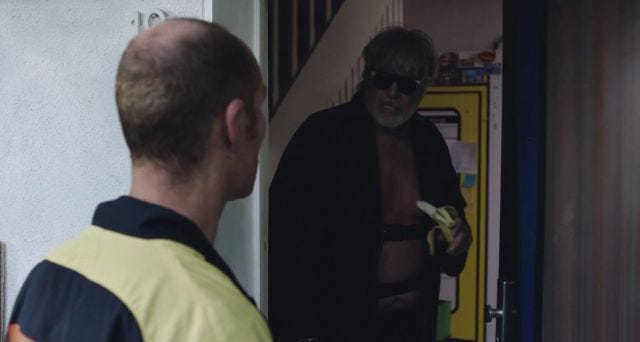 Man answers door to delivery driver in dressing gown with swimming goggles eating a banana