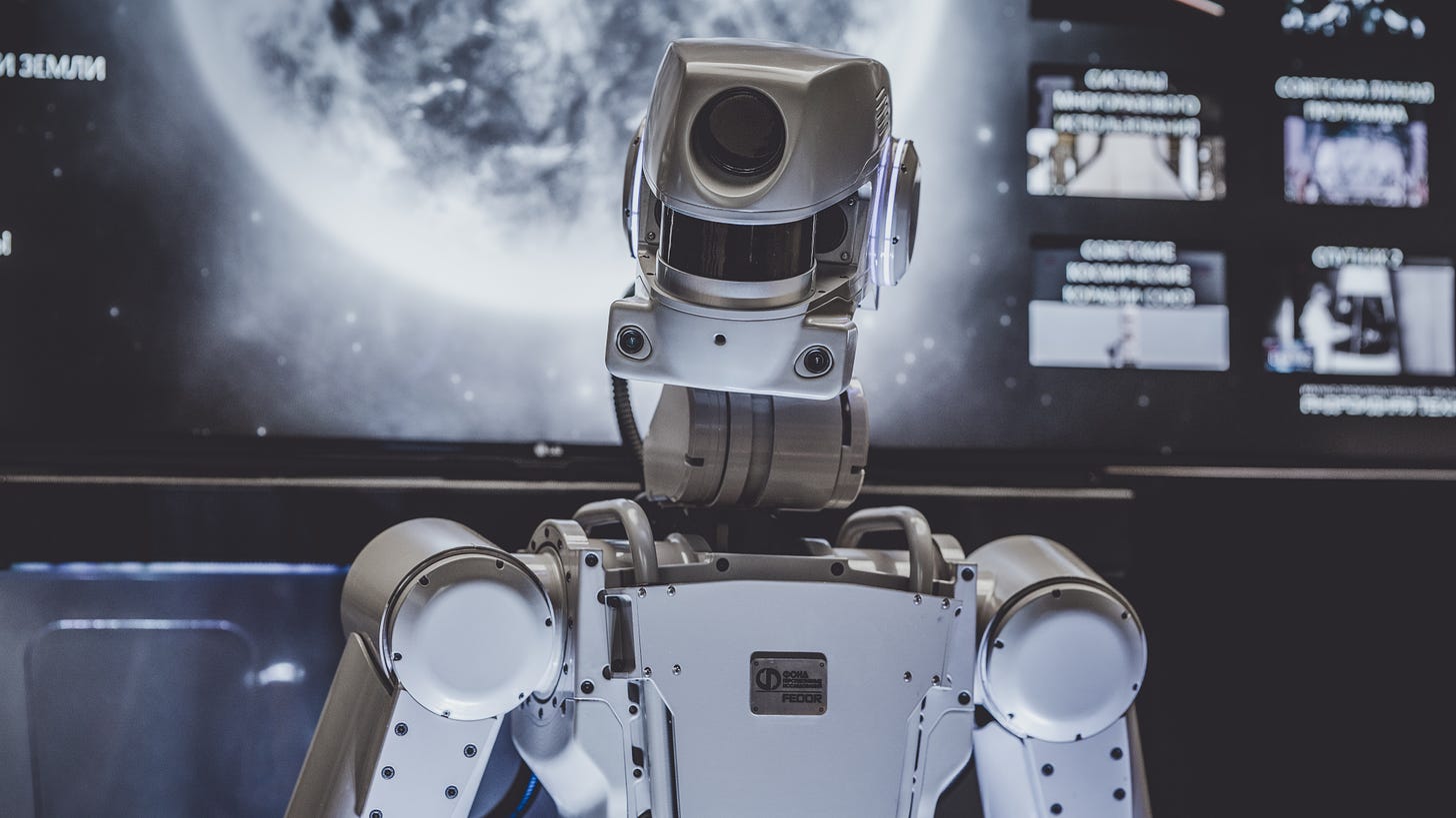 A silver robot in front of a dark screen featuring an image from outer space.