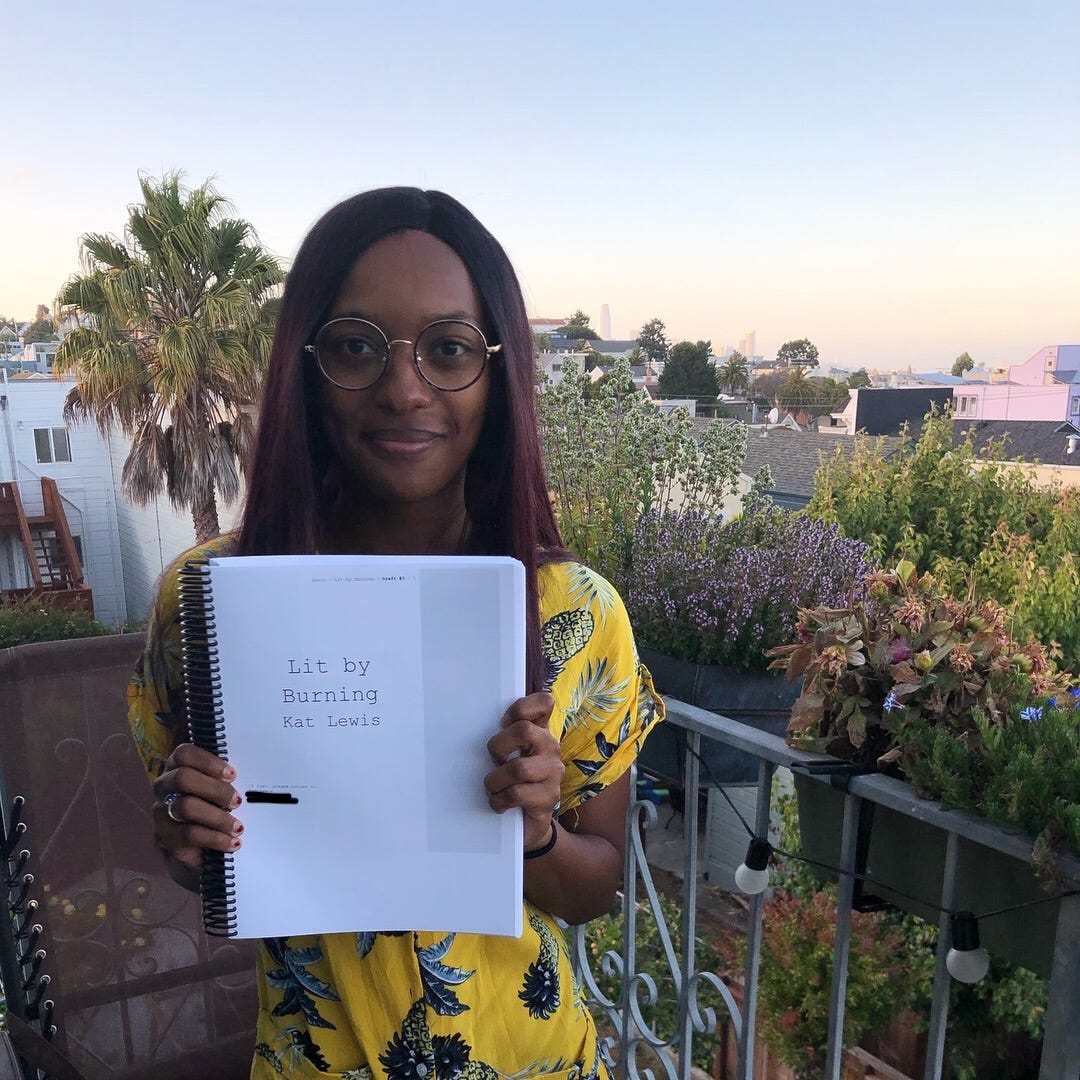 A photo of Kat holding up the printed manuscript for her novel, Lit by Burning.
