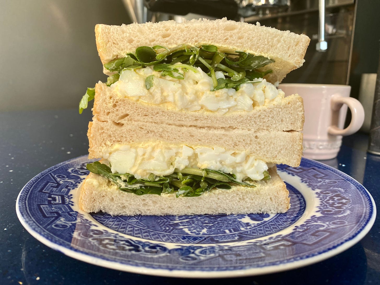 Cross section of an egg mayonnaise sandwich with salad on white bread. Sandwich is on a blue and white plate