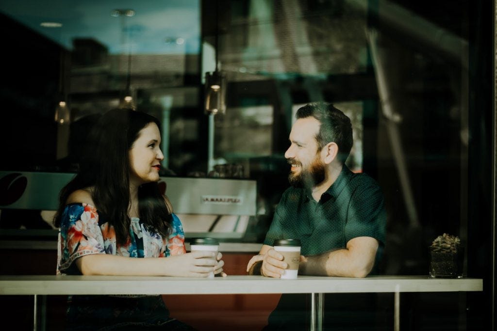 mid-view of two people through a coffee shop window, they are looking at each other and smiling