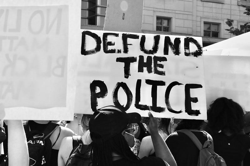 A photo of a protestor holding a Defund the Police sign