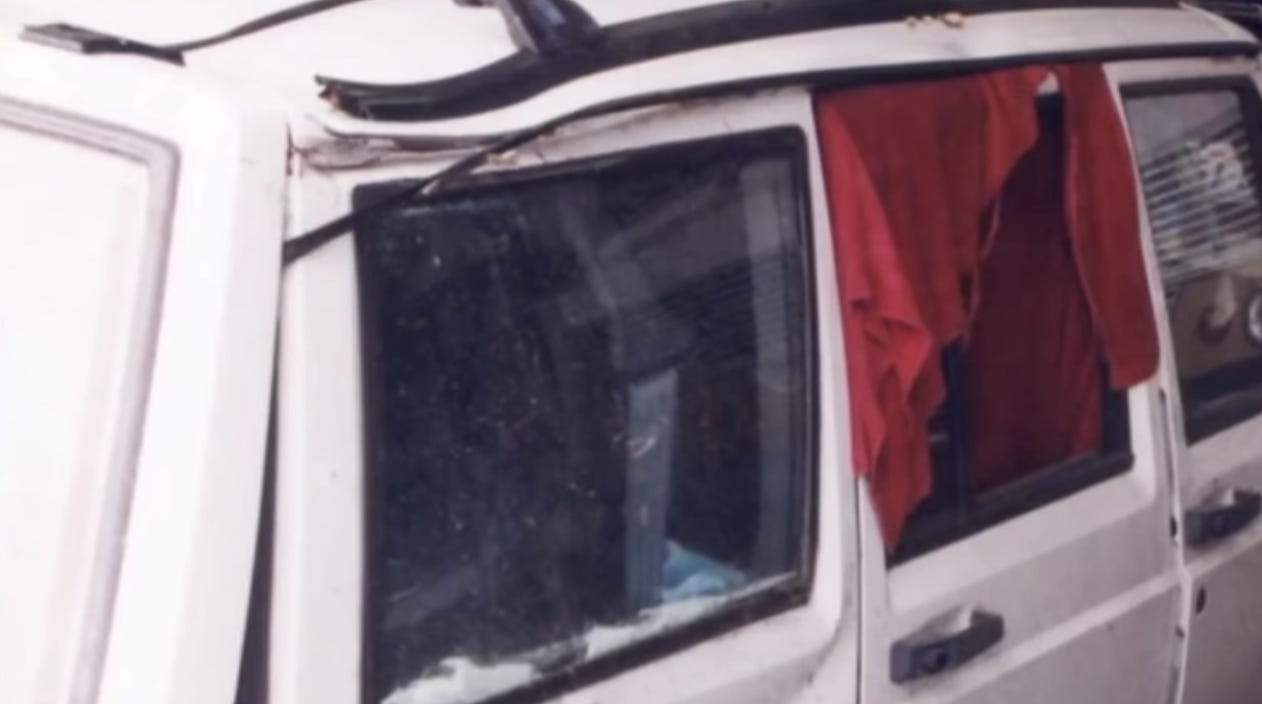 The side of a white vehicle with blankets in the windows and obvious damage to the outside