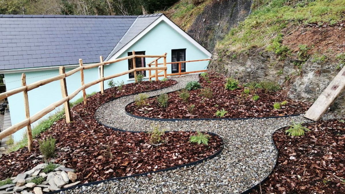 Curvy path on clifftop garden, newly planted, looking back to pale blue house