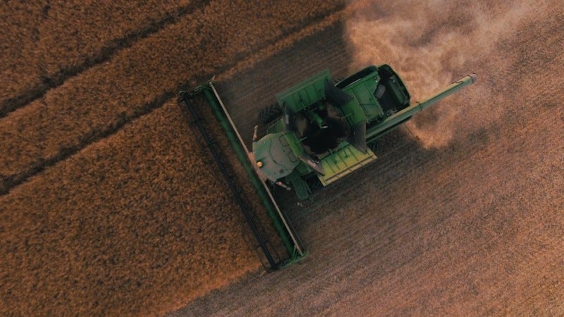 A green tractor harvesting grain, leaving dust in its wake.