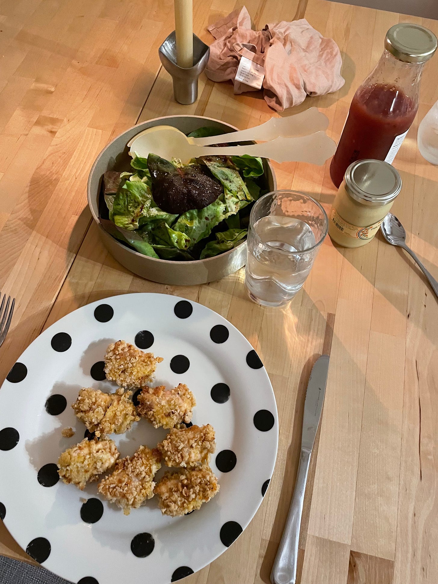 Dining table with a plate of chicken nuggets, green salad, mustard and tomato sauce. A fun meal for adults too.