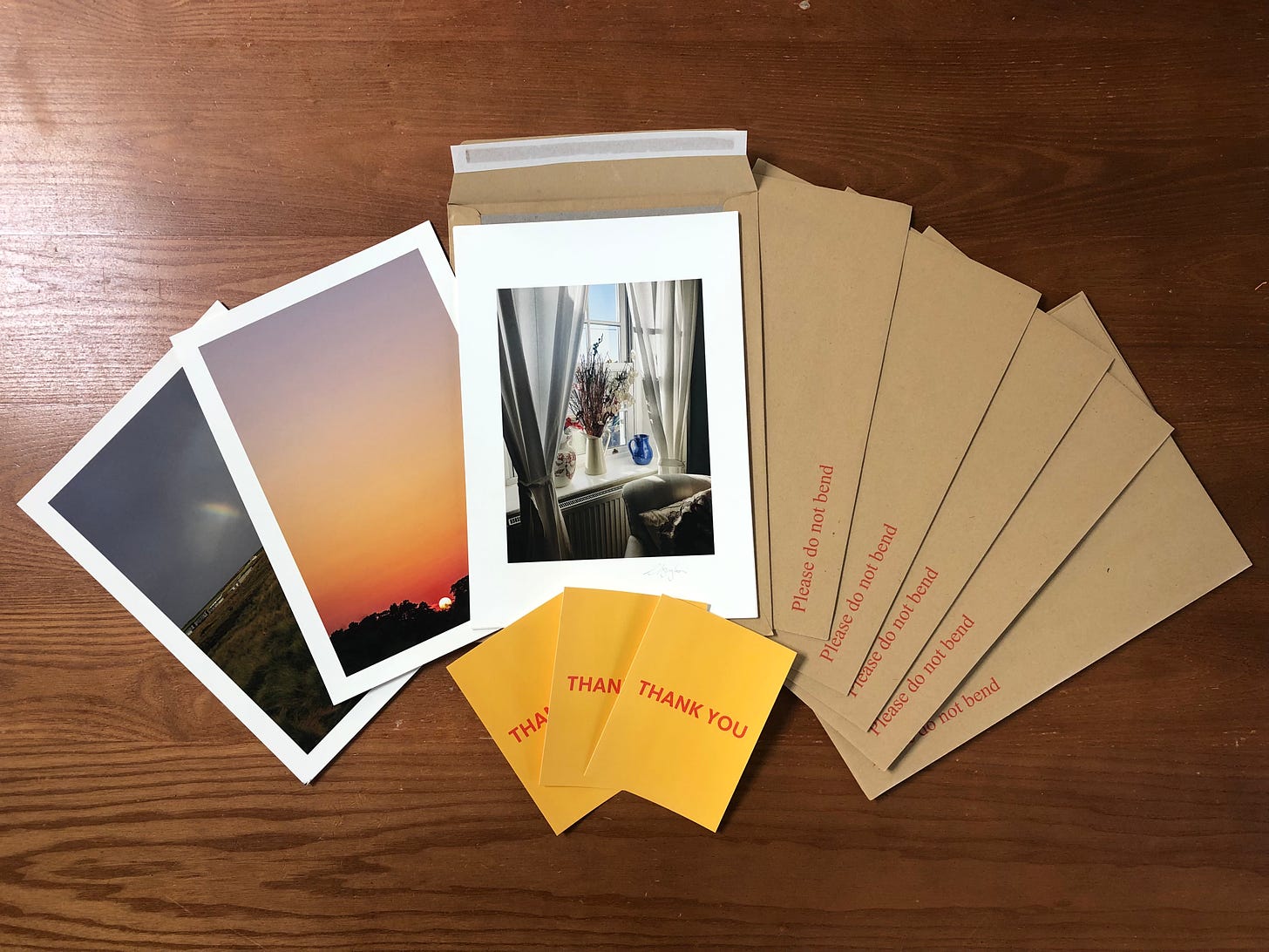 Prints, yellow thank you cards and do not bend envelopes fanned out on a wooden table