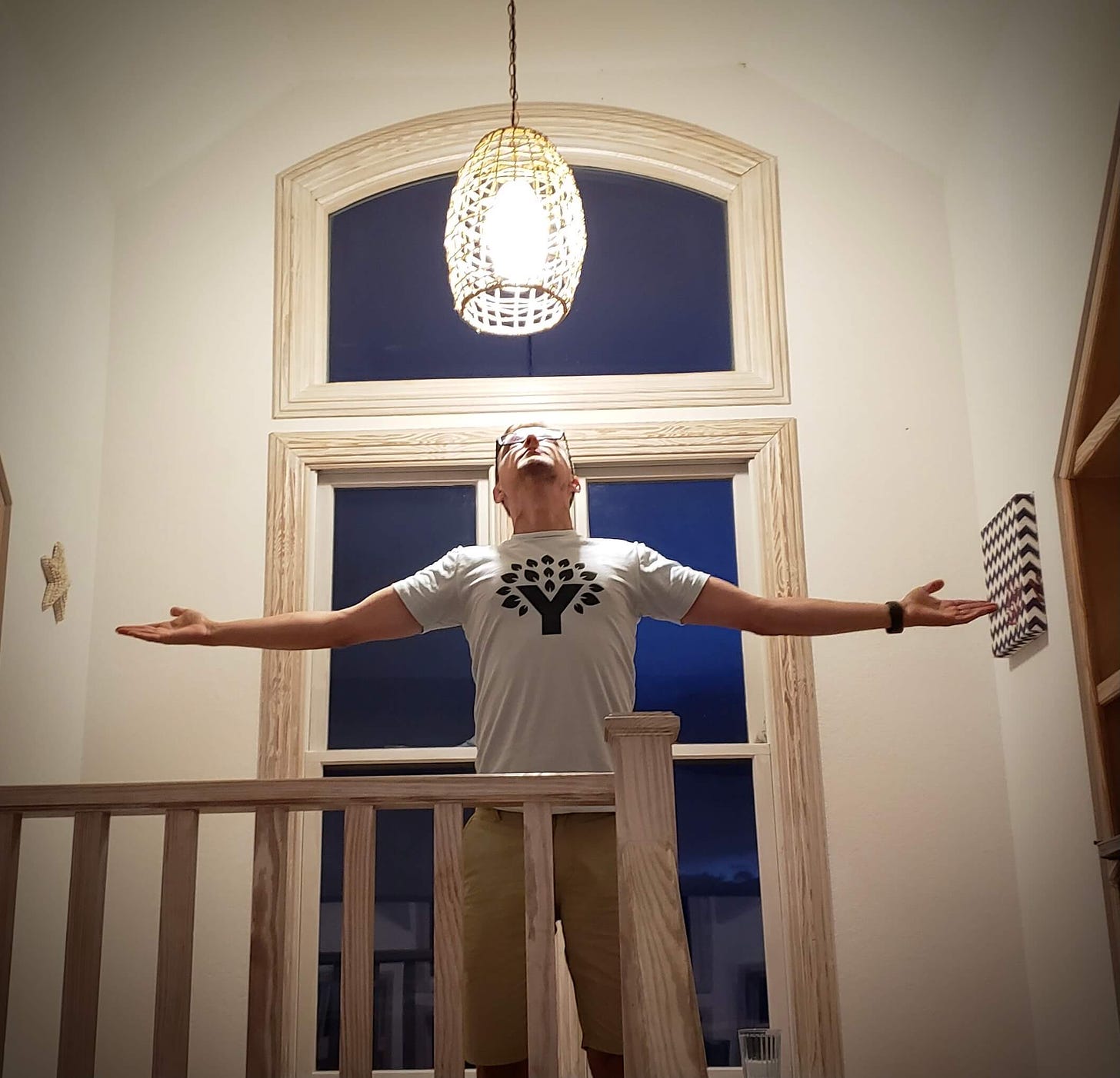 Kyle standing below a light with his arms spread, wearing a YNAB tshirt