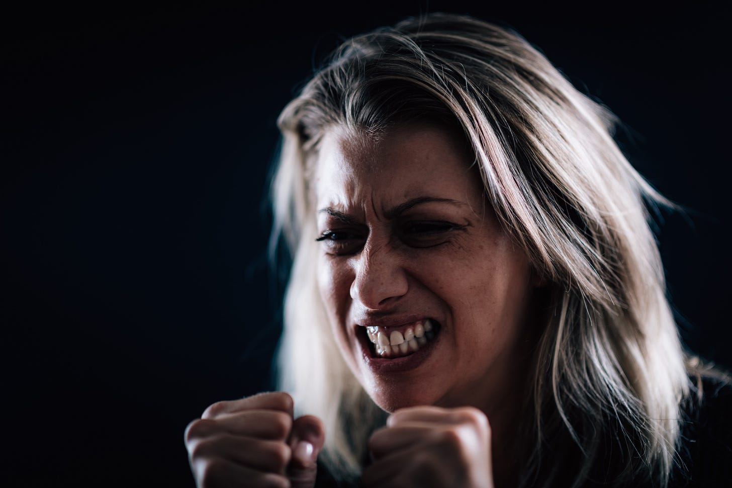 An woman with a mean face scowls and squeezes her fists in anger.