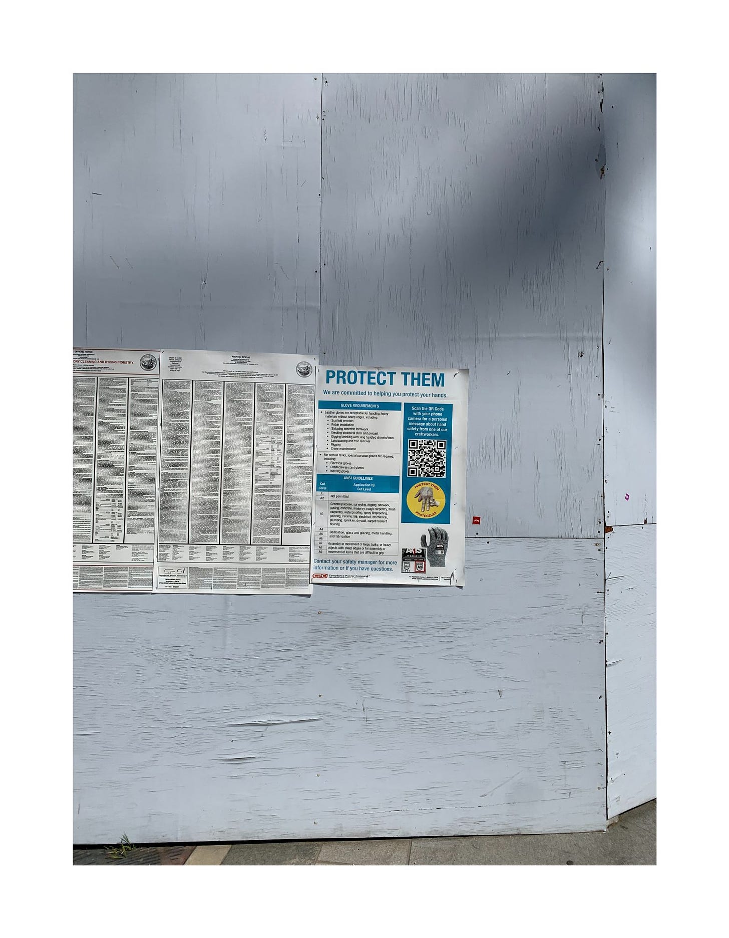 Tall wooden walls covering a construction site feature a few safety notices.