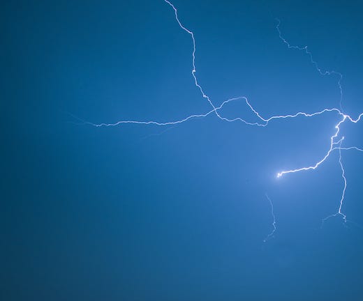 Blue white lightning strikes against a deep blue sky.