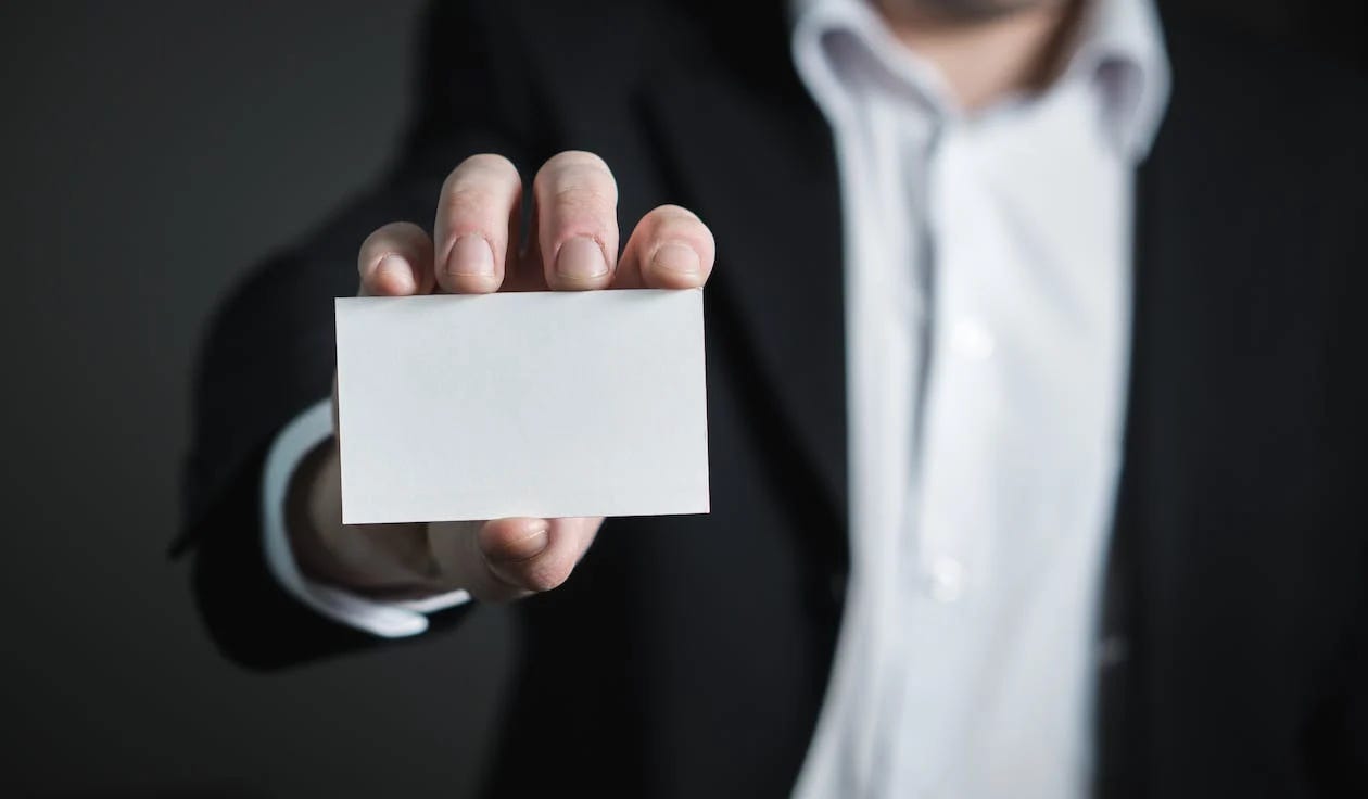 Pexels image by Pixabay of a man in a suit holding up a blank business card.