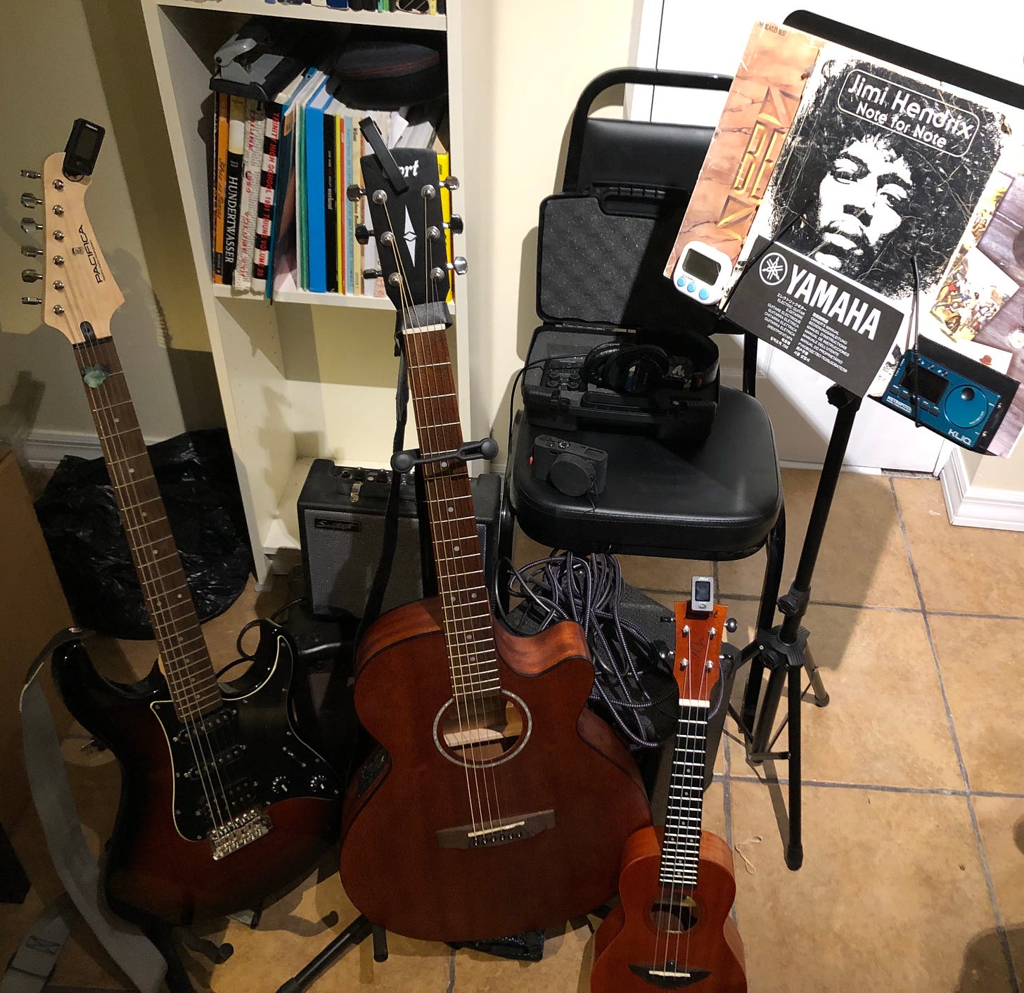 Electric guitar, acoustic guitar, ukulele, amplifier, camera, chair, music stand, and metronome. Recording device and headphones.