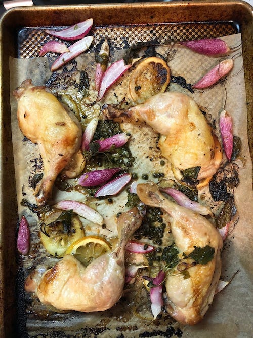 A sheet pan lined with parchment paper filled with roasted chicken quarters and scattered with shallots
