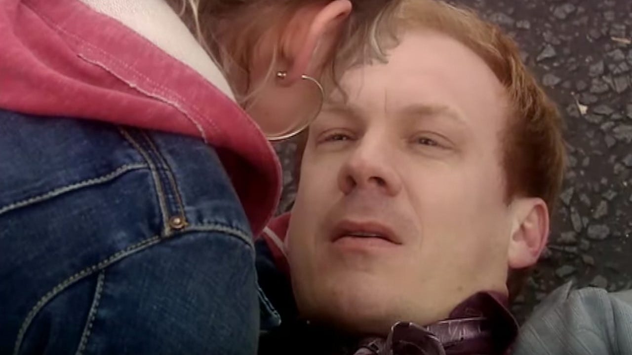 This image shows Rose Tyler (played by Billie Piper) comforting her father, Pete Tyler (played by Shaun Dingwall), as he dies from injuries sustained when a speeding automobile strikes him. Pete lies on the pavement and looks into the eyes of his daughter, whose back is to camera. This image shows Rose Tyler (played by Billie Piper) comforting her father, Pete Tyler (played by Shaun Dingwall), as he dies from injuries sustained when a speeding automobile strikes him. Pete lies on the pavement and looks into the eyes of his daughter, whose back is to camera.